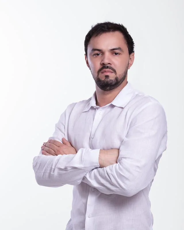Dr. Firminio Humberto em pé, de braços cruzados, de camisa branca